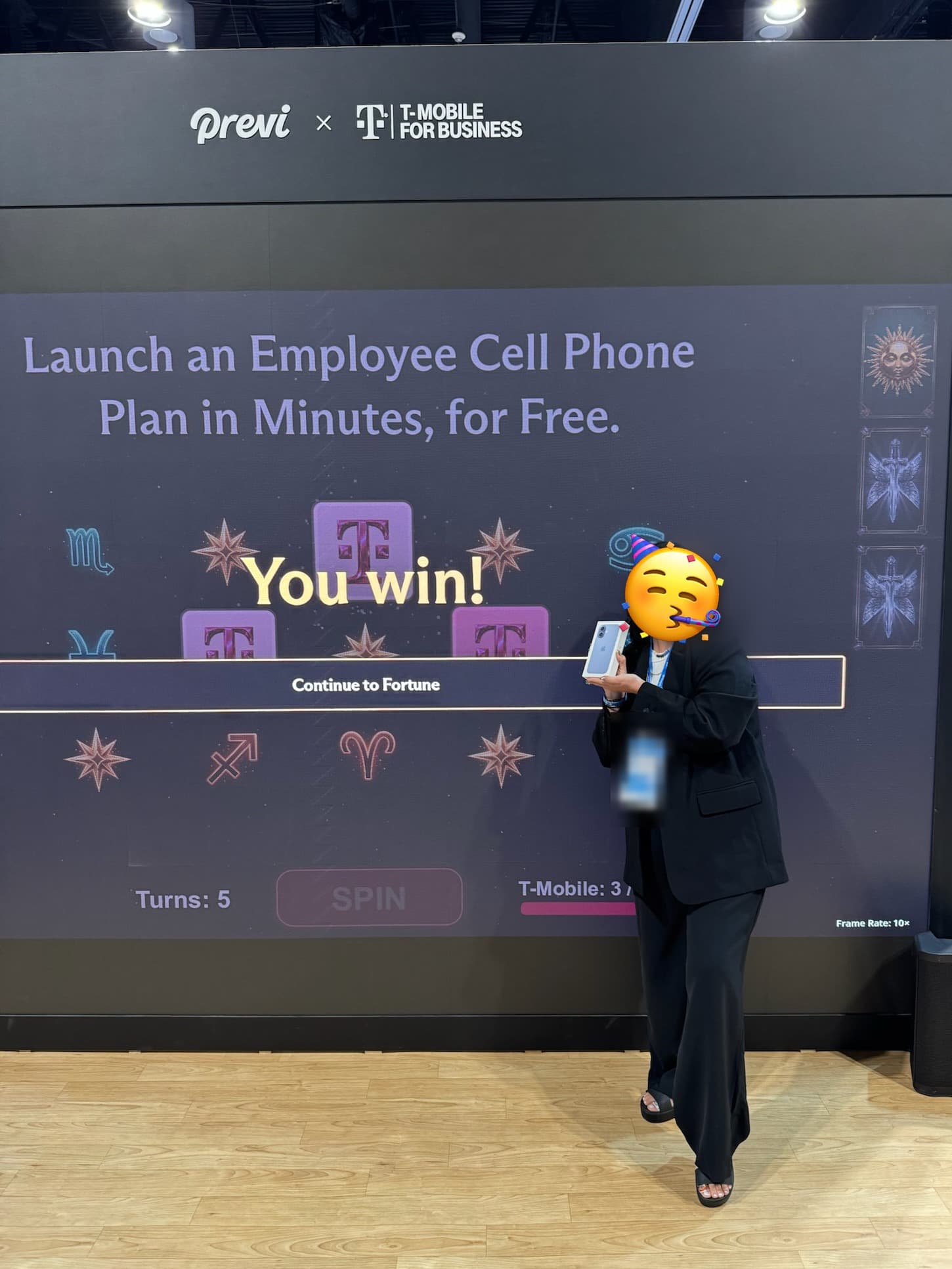 An attendee celebrating after winning an iPhone at the Previ x T-Mobile booth, in front of a You win! screen, face covered with a party-face sticker for privacy